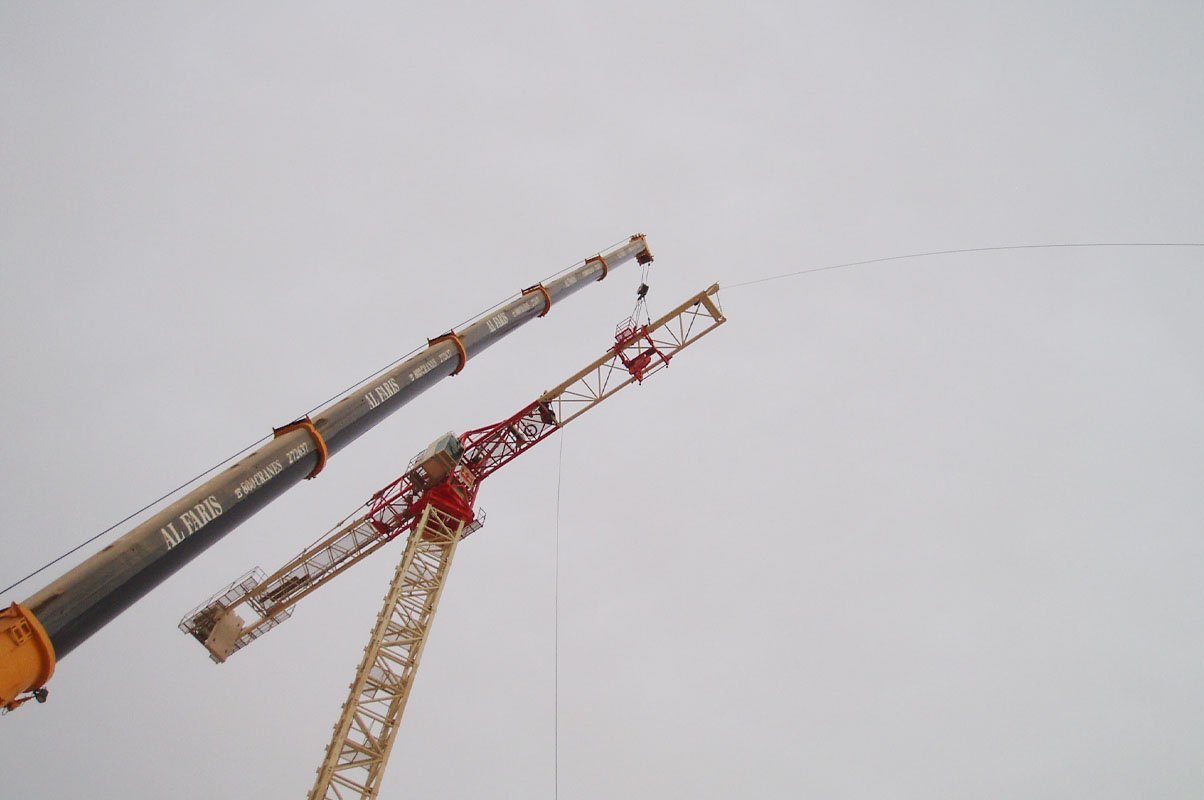 Technicians calibrating safety systems on the upper mechanical section of a tower crane.