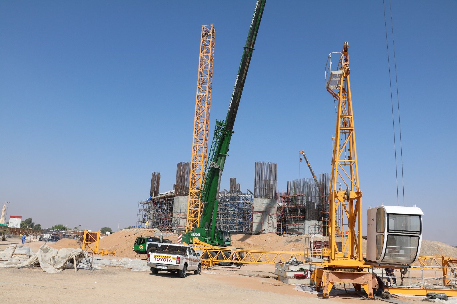 Operational tower crane installation setup with mast sections and support crane on an active site.